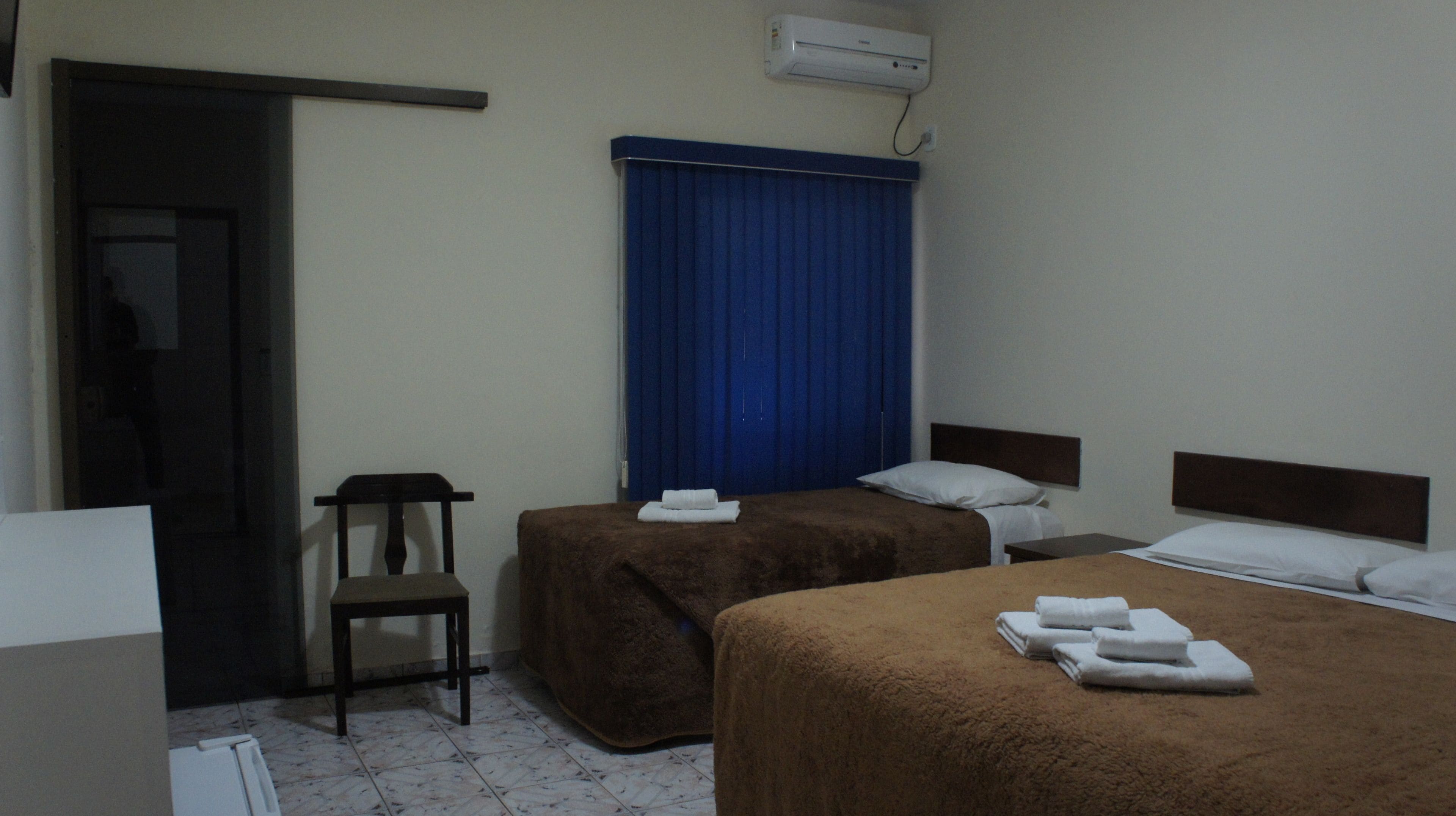 Habitación de hotel con dos camas, una silla, un escritorio y un equipo de aire acondicionado.