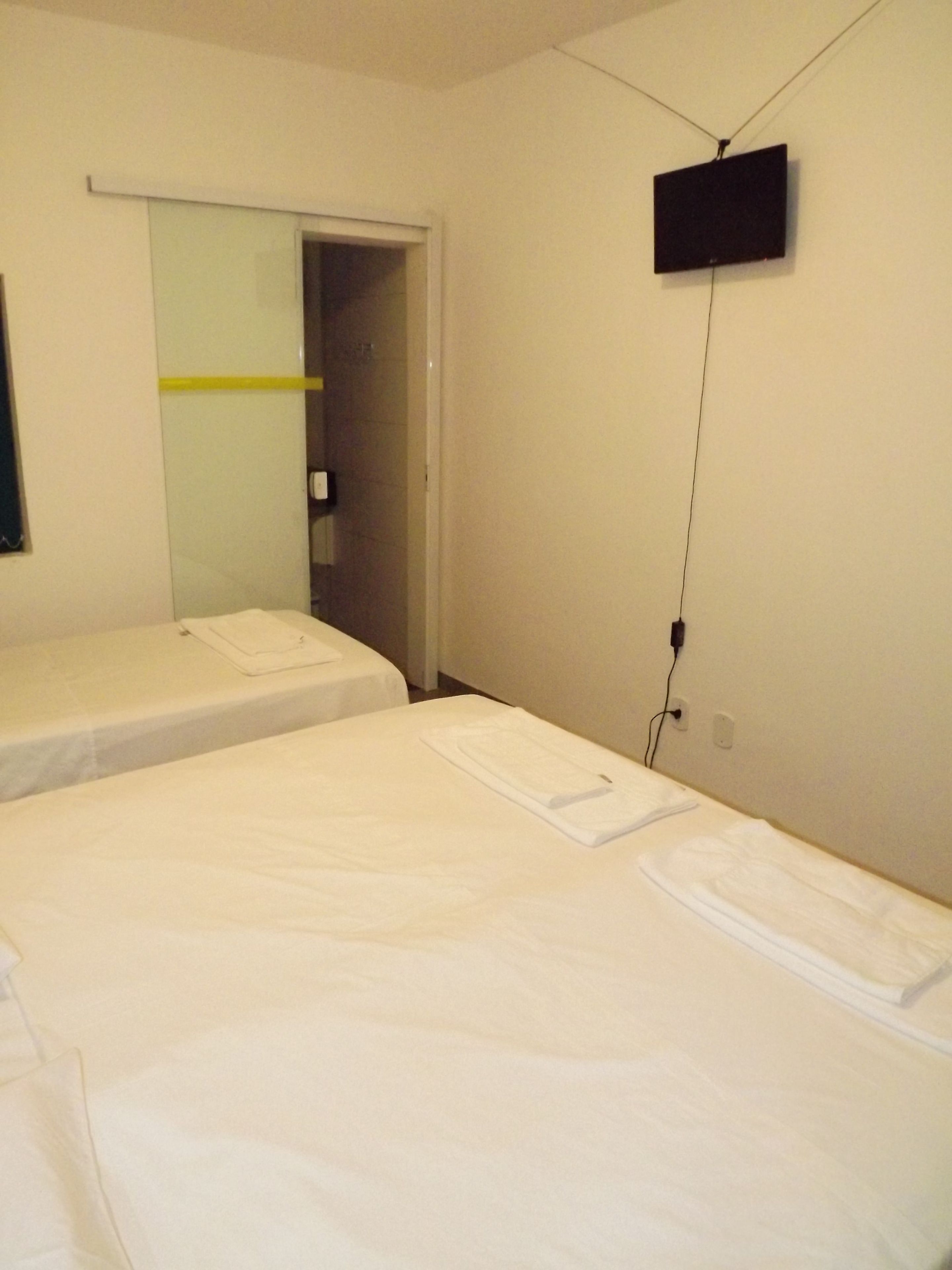 Quarto de hotel com duas camas de solteiro, uma televisão de tela plana na parede e uma porta que dá para o banheiro.