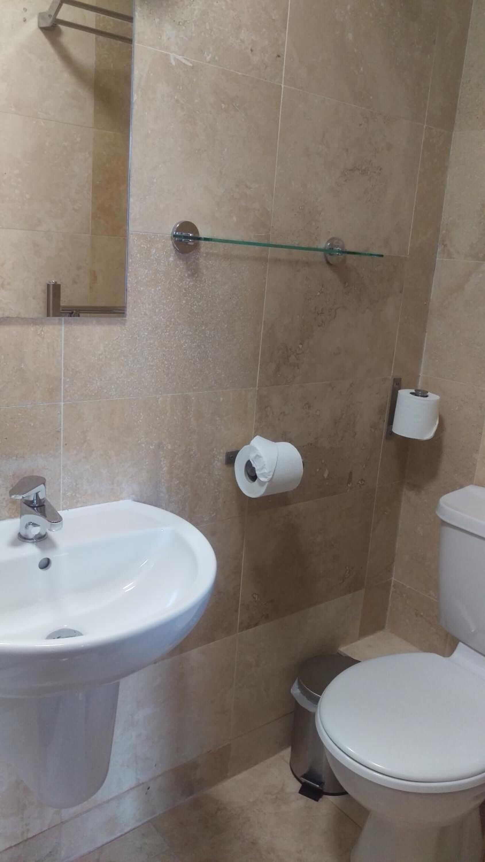 Un baño con un lavamanos blanco, inodoro y dos rollos de papel higiénico en la pared.
