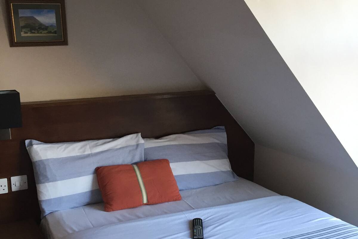 A neatly made bed with striped bedding, a single pillow, and a remote control on the bed.