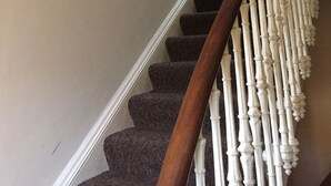 A staircase with a wooden handrail and white balusters, carpeted steps, and framed pictures on the wall. - Cambridge House (Edinburgh)