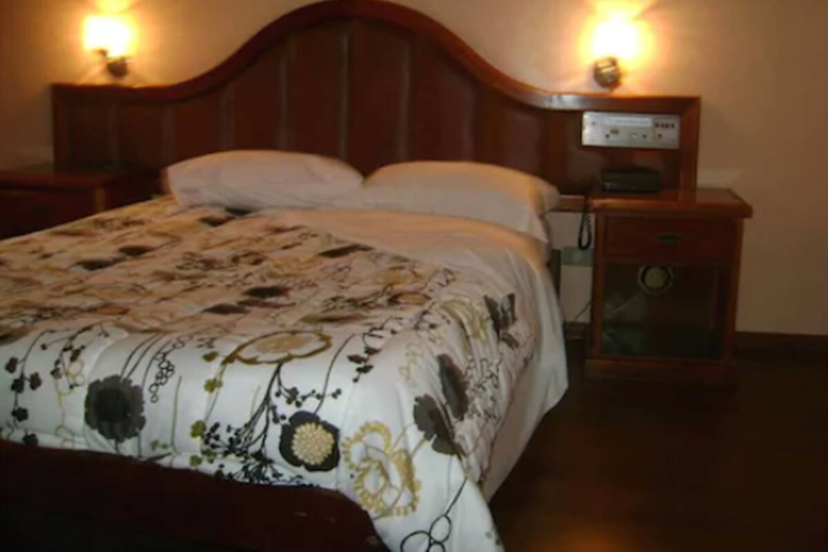 A neatly made bed with a floral bedspread, two bedside lamps, and a nightstand with a clock.