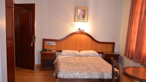 A wooden bed with a headboard, a bedside table, a nightstand, a chair, and a small table.