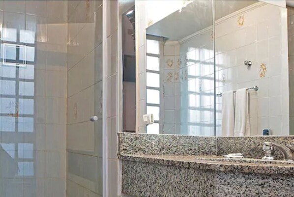A bathroom with a granite countertop, a glass shower enclosure, and a mirror reflecting the room.