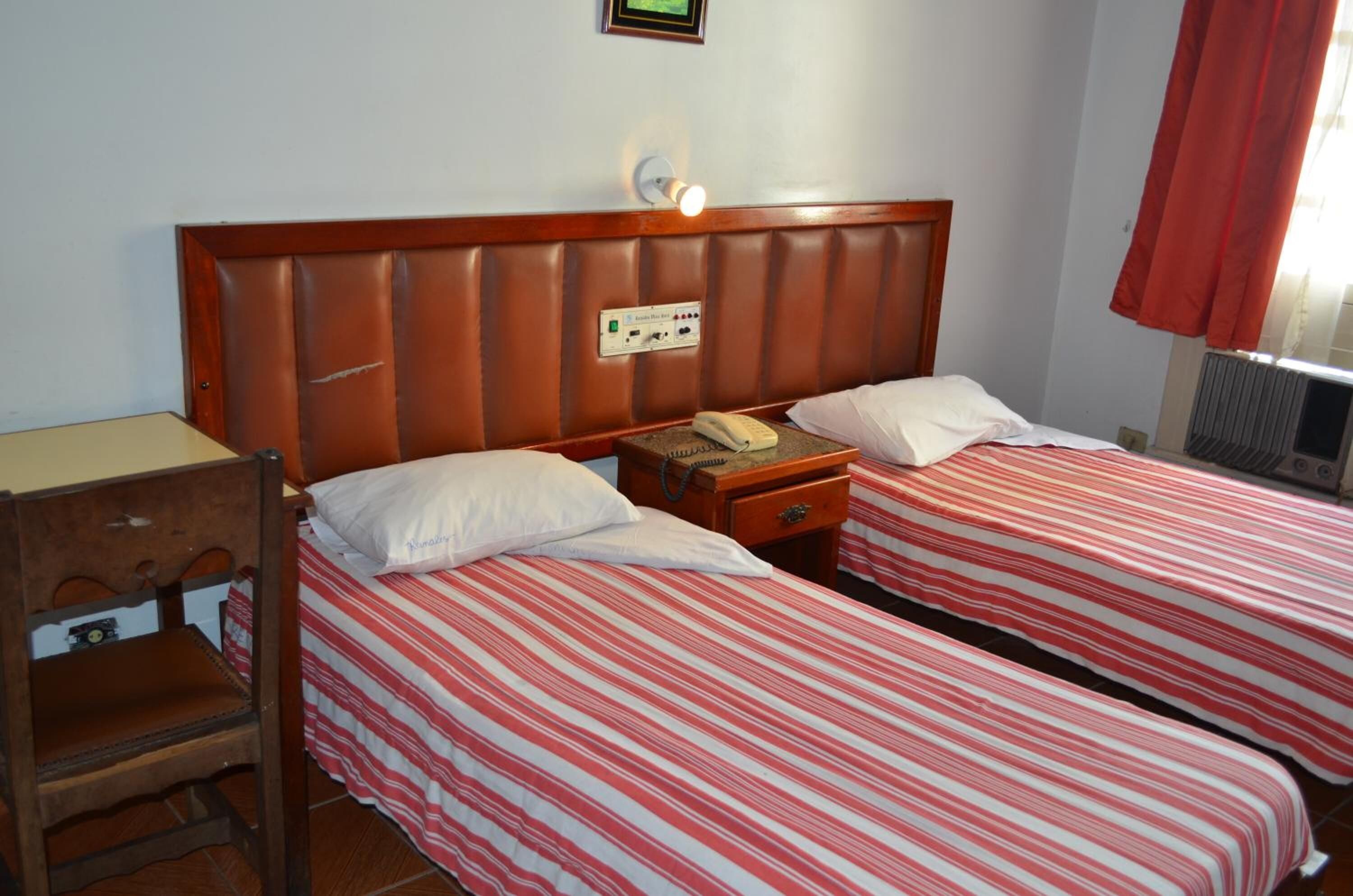 A hotel room with two beds, a wooden nightstand, a telephone, and a wall-mounted light fixture.