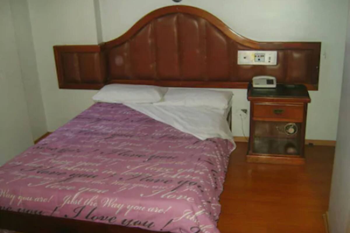 A bedroom with a wooden headboard, a bed with a purple bedspread, white pillows, and a nightstand with a radio.