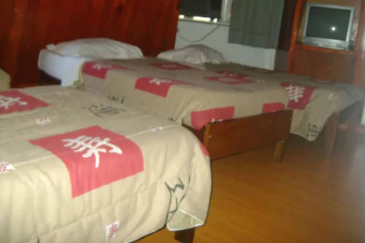 A room with two beds, each with a beige bedspread and red accents, wooden headboards, and a television on a wooden stand.