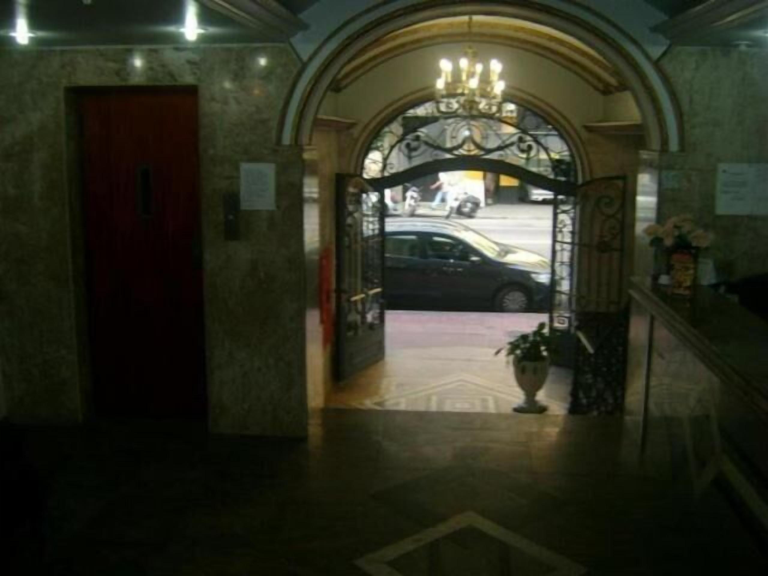 Un vestíbulo con piso de mármol, una puerta roja y un arco decorativo con candelabro.