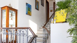 A staircase with a wooden handrail and metal balusters, leading to a landing with a glass-fronted cabinet and framed artwork on the walls. - B&B Alma (Lucca)