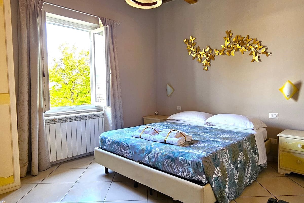 Un dormitorio con cama, mesitas de noche, una ventana con cortinas y un adorno en la pared.