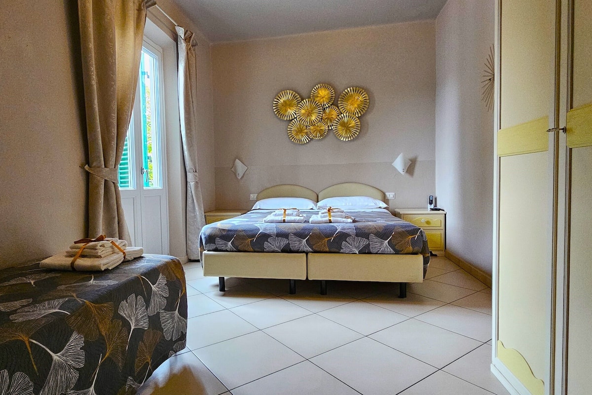 Un dormitorio con cama, mesita de noche, lámpara y ventana con cortinas.
