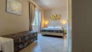 A bedroom with two beds, a window with curtains, a wall-mounted light fixture, and a decorative wall piece. - B&B Alma (Lucca)
