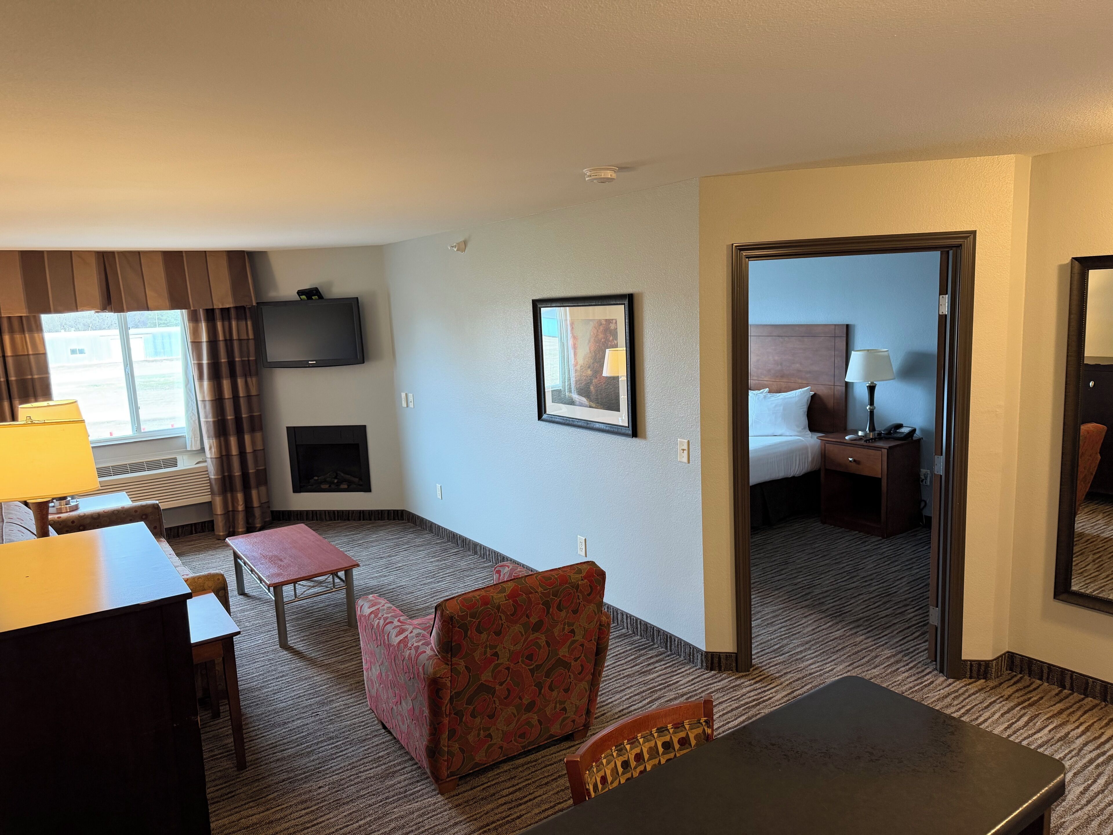 Een hotelkamer met een televisie, open haard, ingelijst kunstwerk, bed, bureau, stoel en uitzicht op buiten.