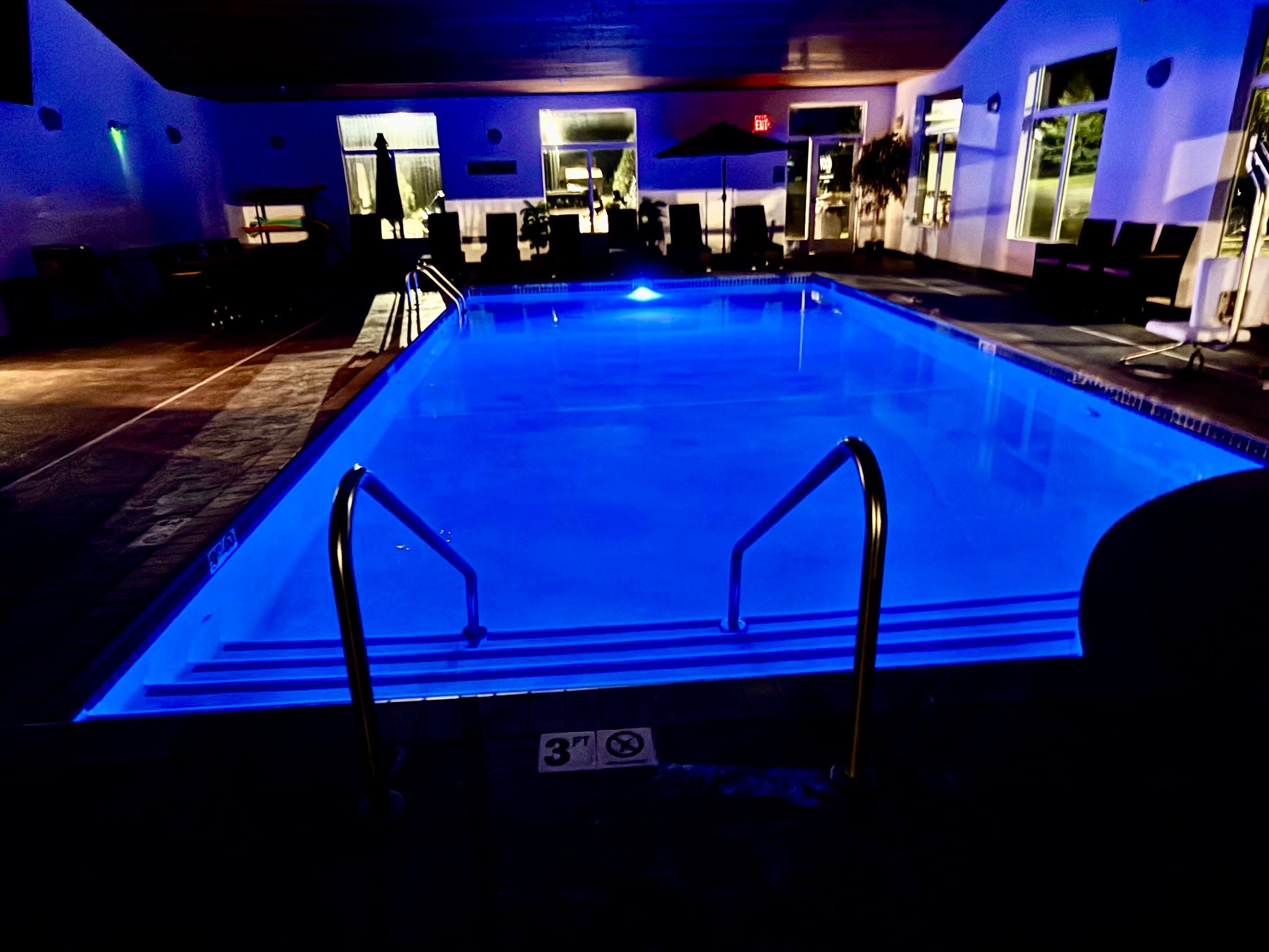 A swimming pool with a blue light, lounge chairs, and a sign indicating a 3ft depth.