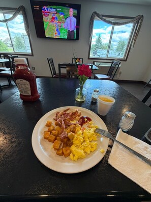 A breakfast plate with eggs, bacon, and hash browns on a table with a bottle of ketchup and a vase of flowers. - American Inn & Suites (Parkers Prairie)