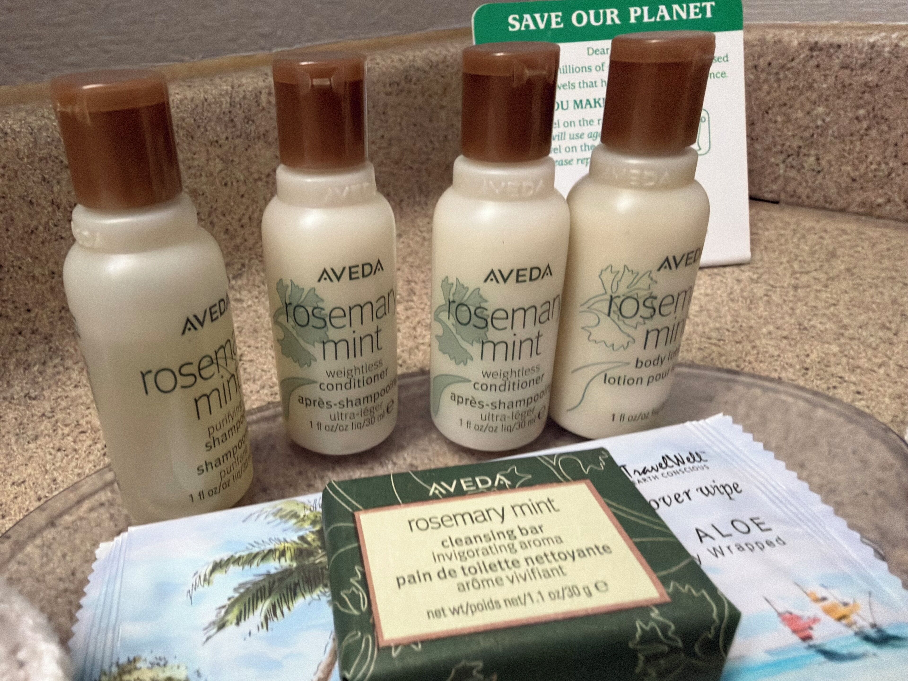 Four bottles of Aveda rosemary mint products and a bar of Aveda aloe body lotion on a countertop.
