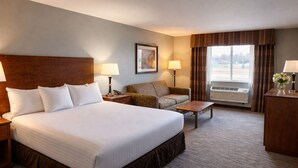 Ein Hotelzimmer mit einem großen Bett, einem Sofa, einem Couchtisch, einem Schreibtisch und einem Fenster mit Vorhängen.