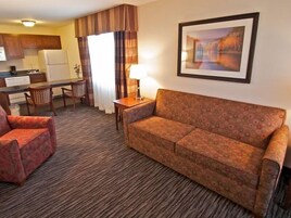 A hotel room with a sofa, armchair, dining table, and a kitchen area.