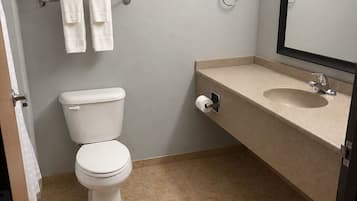 A bathroom with a toilet, sink, mirror, towel rack, and toilet paper dispenser.