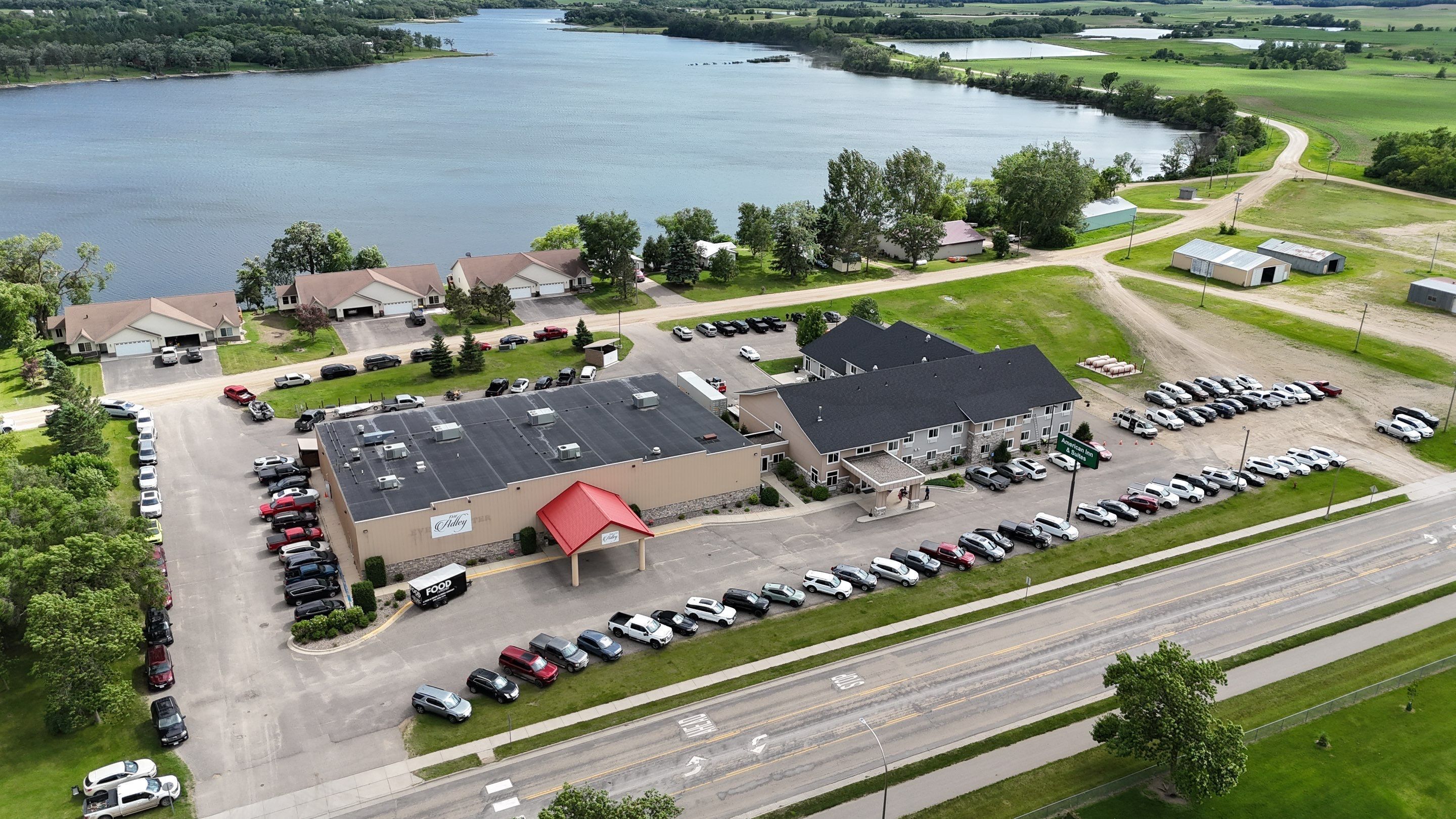 Luchtbeeld van een bedrijfsgebouw met een parkeerplaats, omringd door groen en water.