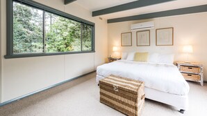 Une chambre avec une grande fenêtre, un lit, des tables de chevet et une commode.