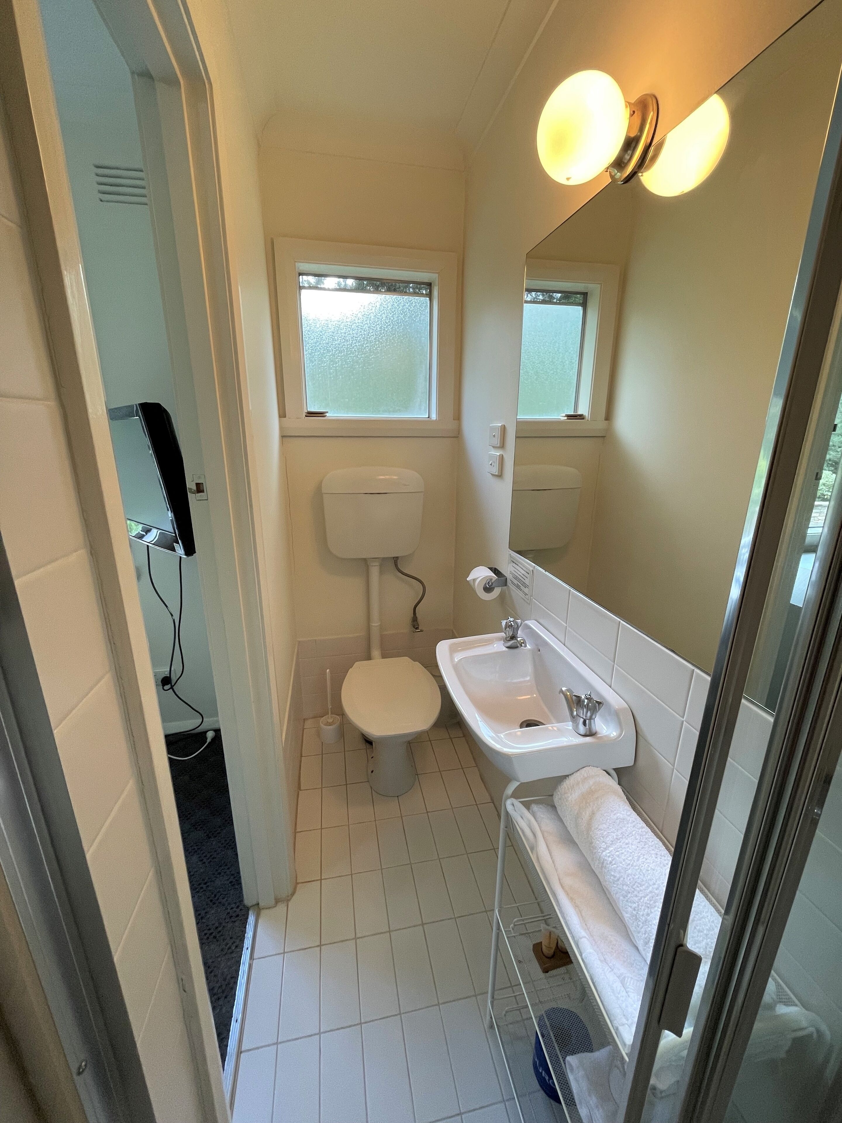 Een kleine badkamer met toilet, wastafel en een klein raam.