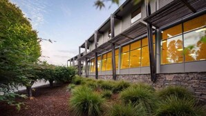 Un bâtiment moderne doté de grandes fenêtres, d’une façade en pierre et d’un espace paysager agrémenté d’arbustes.