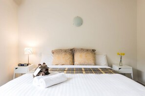 A neatly made bed with a patterned bedspread, two pillows, a bedside lamp, a small table with a vase of flowers, and a teddy bear on the bed. - Panorama Retreat & Resort (Kalorama)