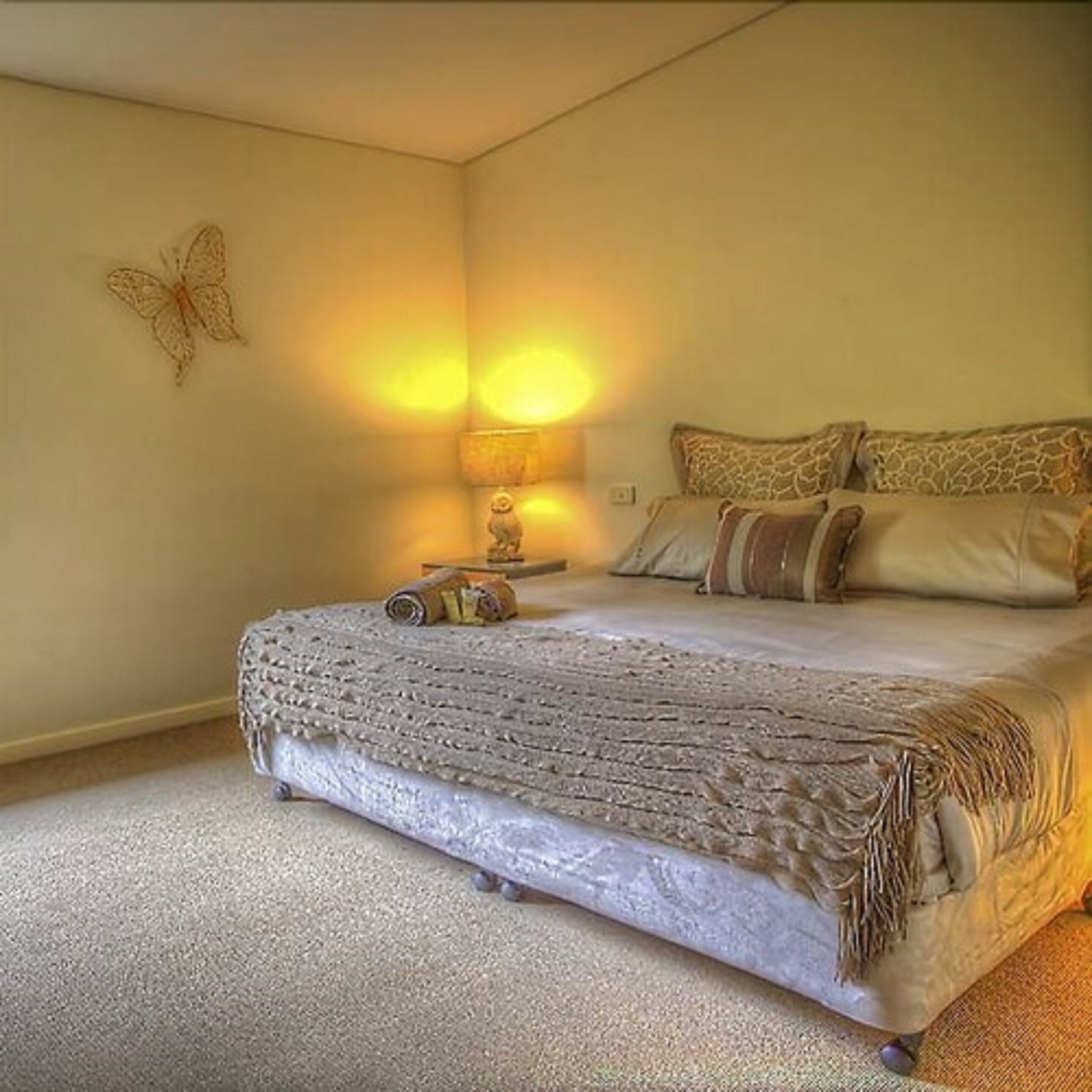 Un dormitorio con cama, almohadas, una lámpara y un adorno en la pared.