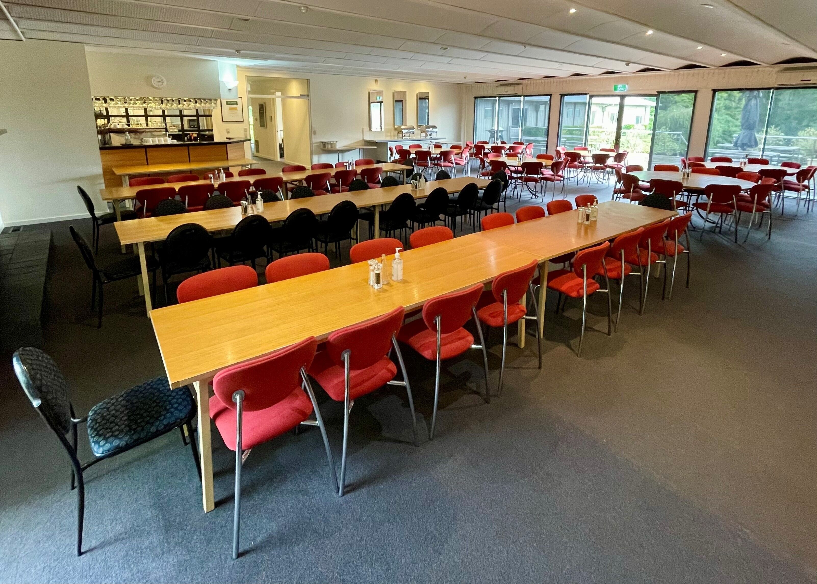 A conference room with multiple tables and chairs, a kitchenette, and large windows.