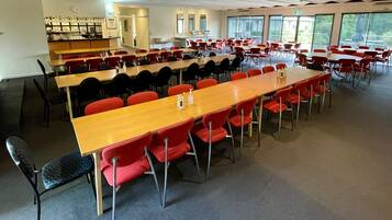 A conference room with multiple tables and chairs, a kitchenette, and large windows.