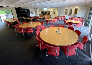 A spacious indoor dining area with round wooden tables and red chairs, a kitchen in the background, and large windows allowing natural light. - Panorama Retreat & Resort (Kalorama)