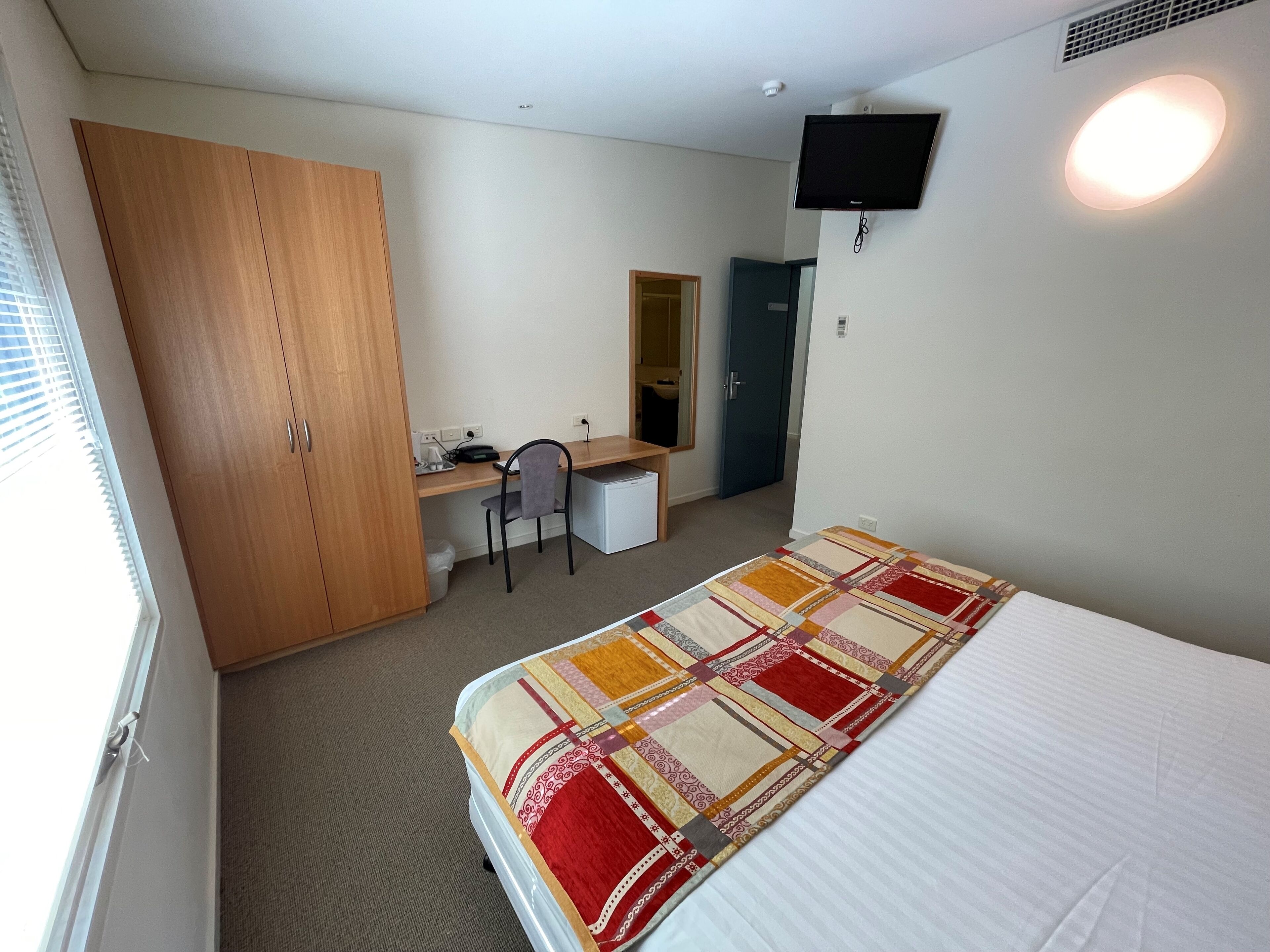 Een slaapkamer met een bed, een bureau, een stoel, een kledingkast en een televisie.