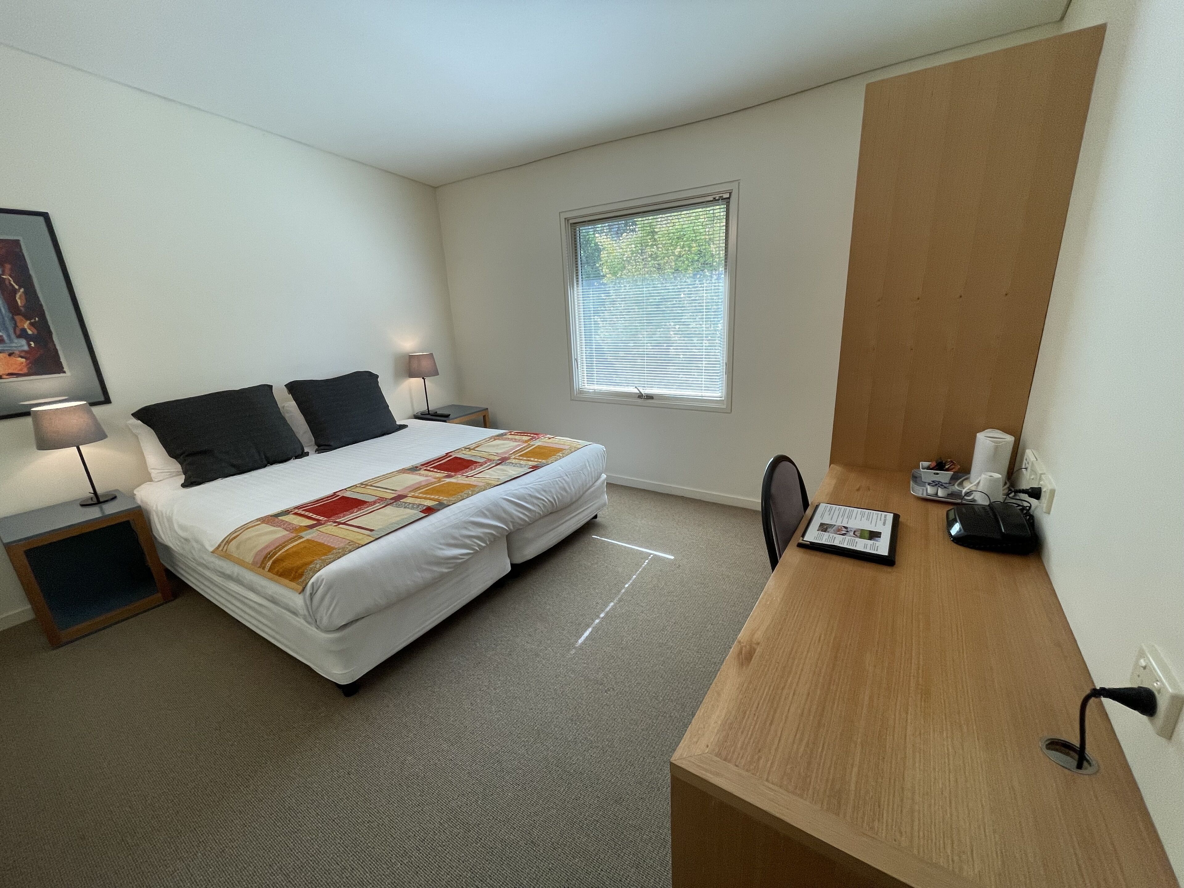 A bedroom with a bed, bedside tables, a desk, and a window.