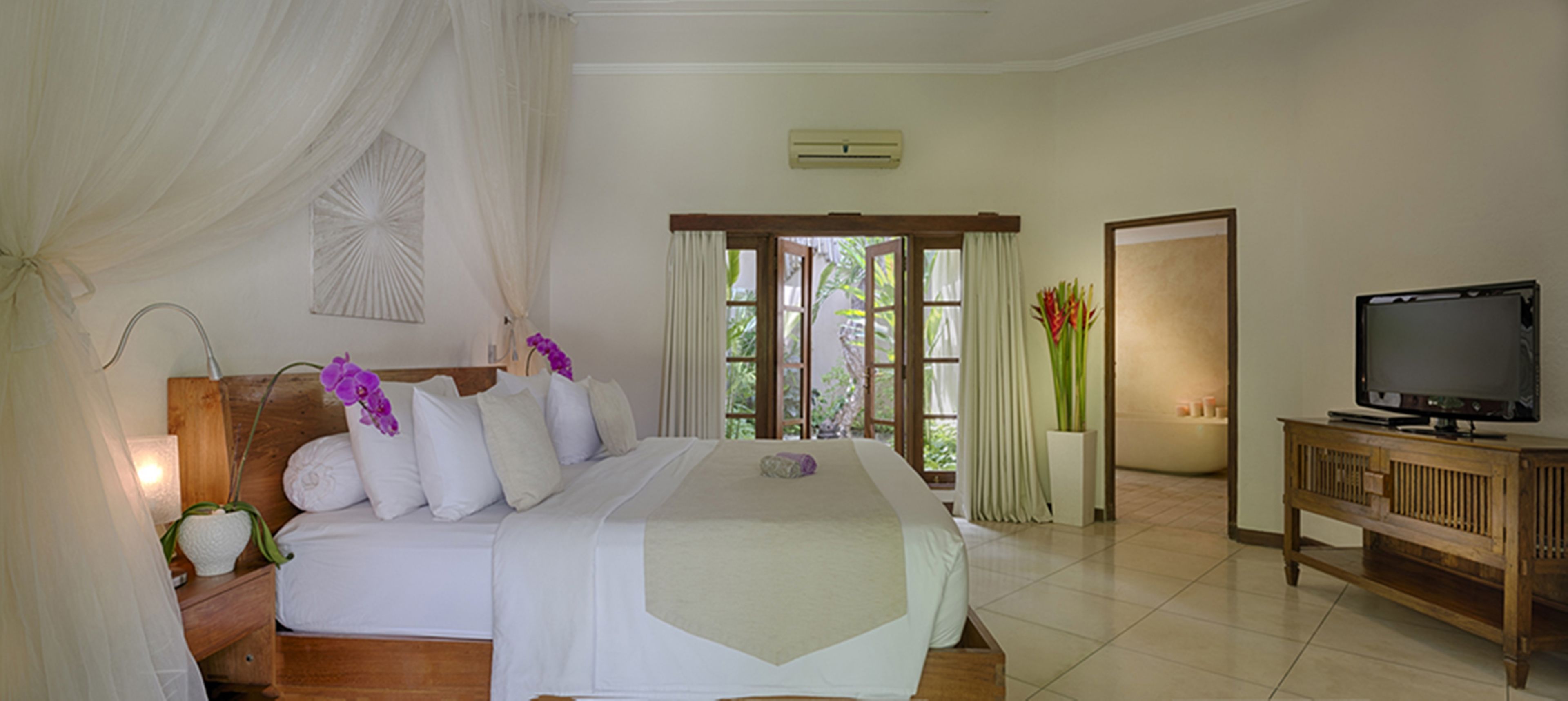 A bedroom with a bed, a television on a wooden cabinet, and a window with curtains.