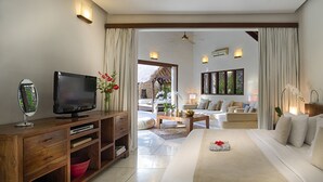 A modern living room with a flat-screen TV, wooden entertainment unit, and a sofa with white cushions. - Villa Kubu, Seminyak (Seminyak)