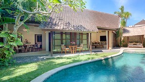 A private pool with a tiled roof, surrounded by lush greenery and a patio area with outdoor furniture. - Villa Kubu, Seminyak (Seminyak)