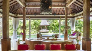 A spacious dining area with a wooden table and chairs, a view of a pool and garden, and a gazebo in the background. - Villa Kubu, Seminyak (Seminyak)