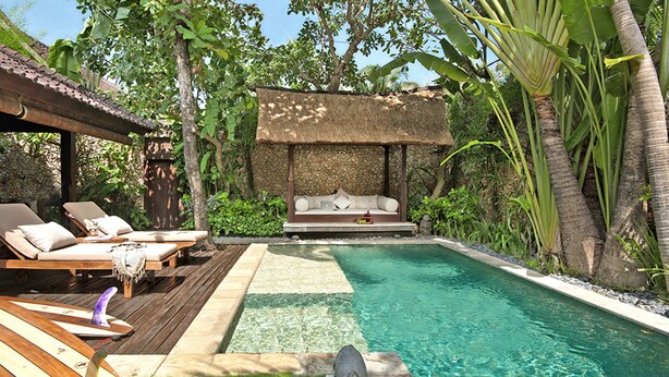 A pool area with lounge chairs, a thatched-roof seating area, and a stone sculpture. - Villa Kubu, Seminyak (Seminyak)