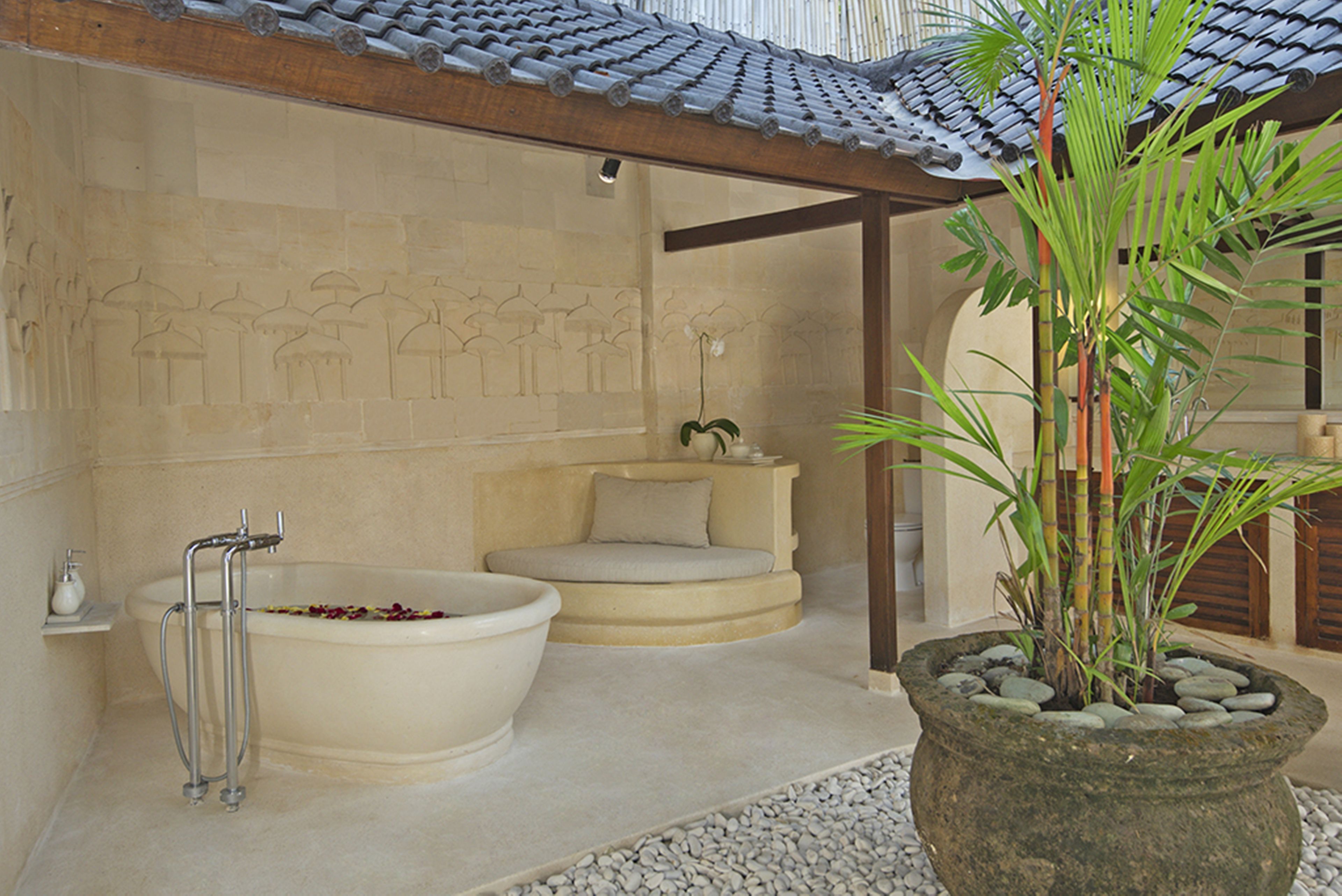 A bathroom with a large bathtub, a small seating area, and a stone planter with a plant.