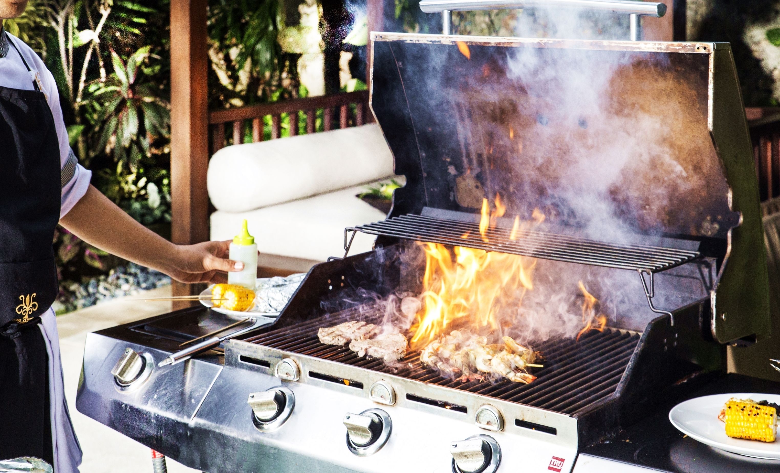 A person grilling food on an outdoor grill with multiple burners and a lid.