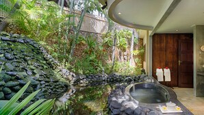 A bathroom with a stone wall, a hot tub, and a wooden door. - Villa Kubu, Seminyak (Seminyak)