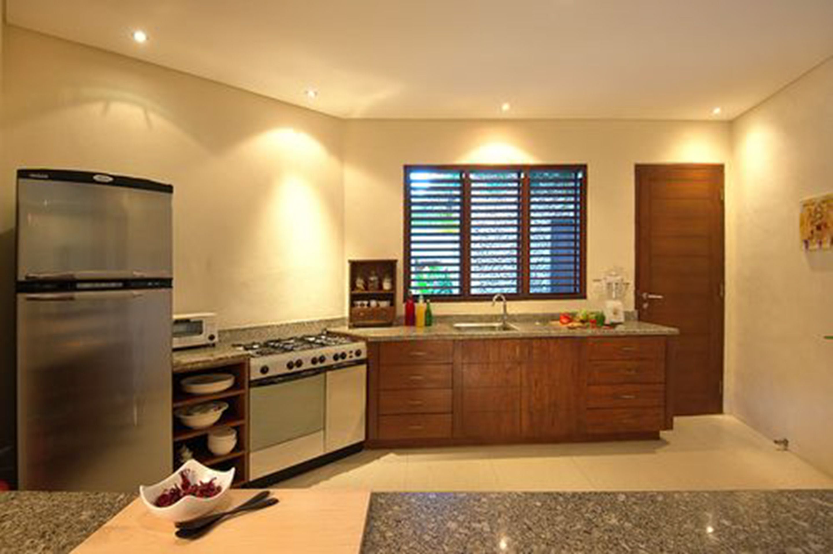 Eine moderne Küche mit Edelstahlkühlschrank, Gasherd, Holzschränken und einer Arbeitsplatte aus Granit.