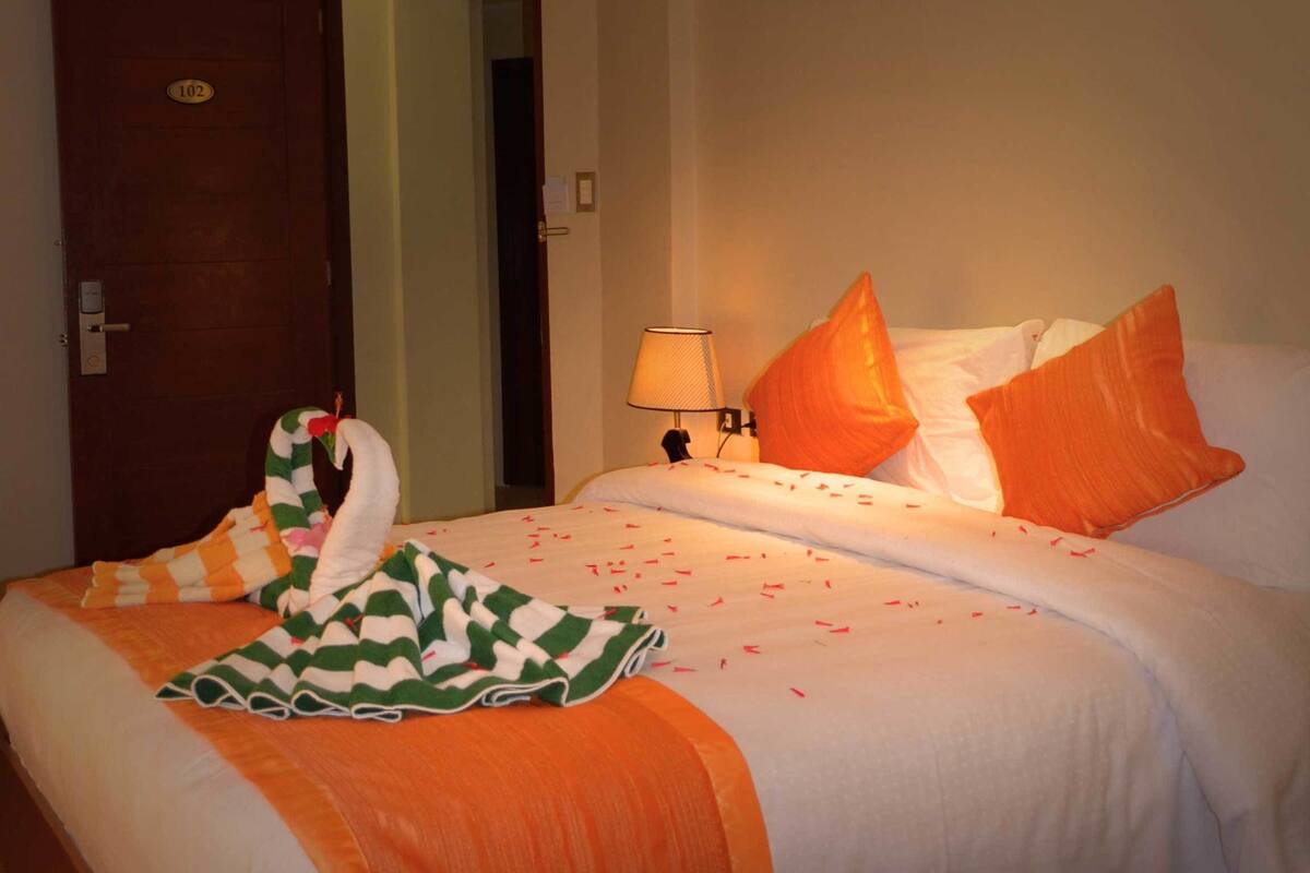 Una habitación de hotel con una cama, una mesita de noche con lámpara y una puerta con el número 102.