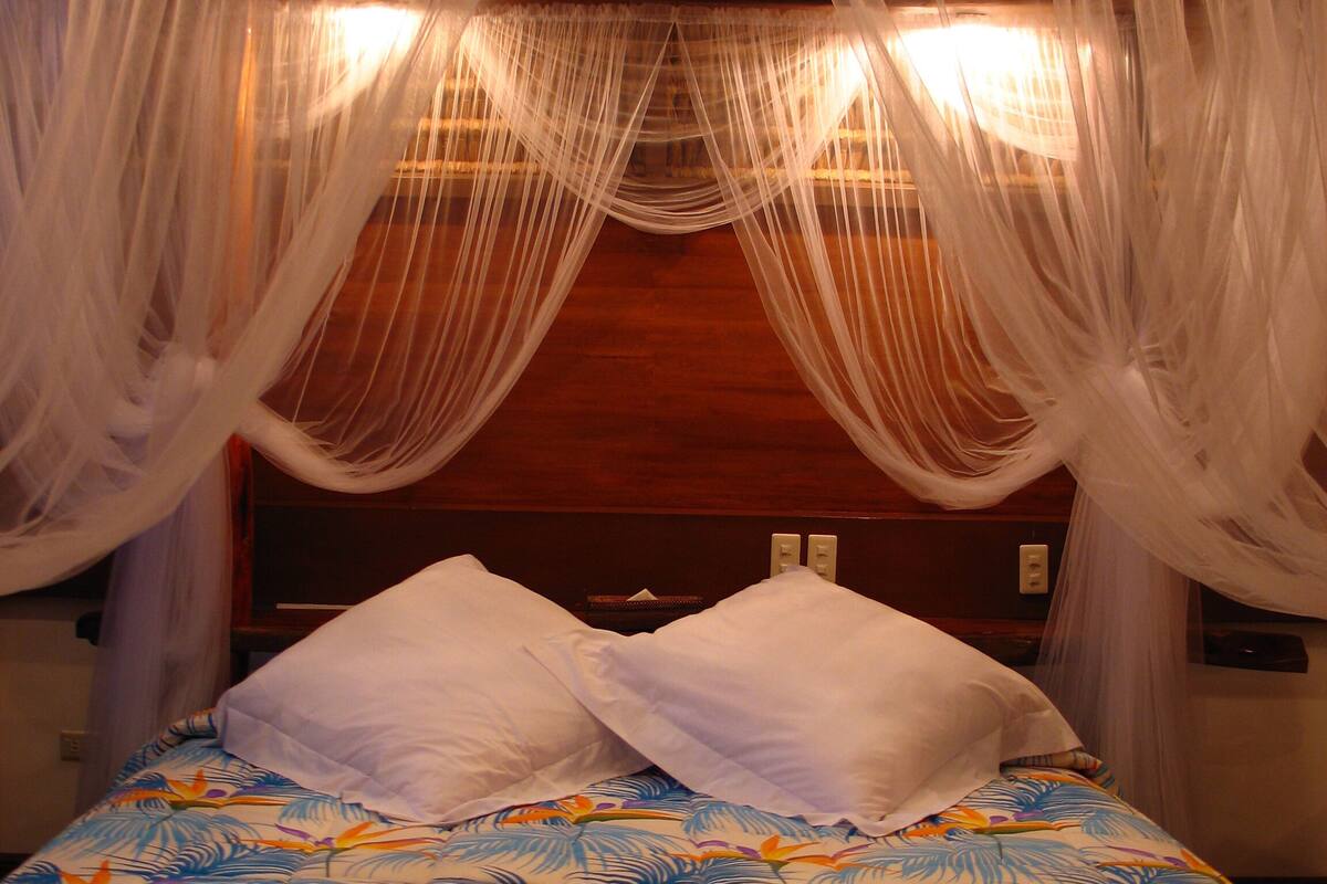 Una cama con colcha estampada de flores, almohadas blancas y cabecera de madera.