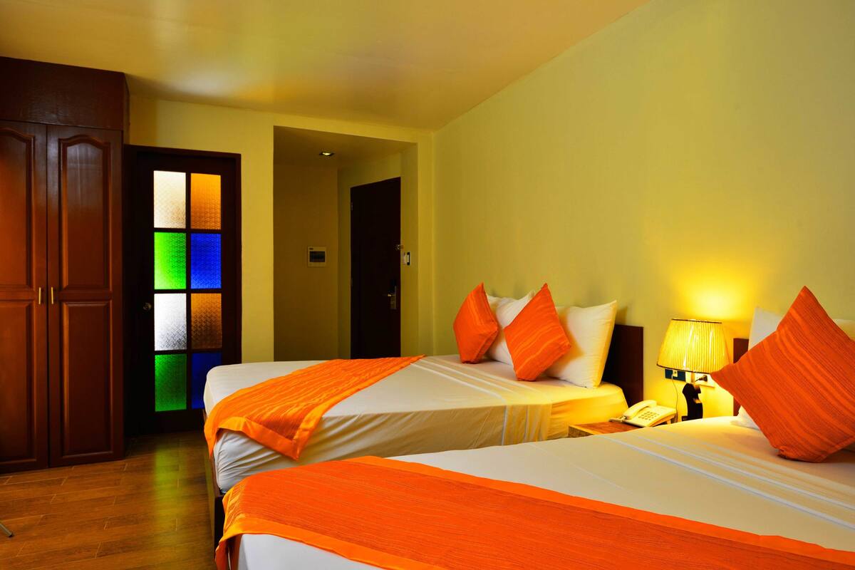 Habitación de hotel con dos camas, armario de madera y una puerta con paneles de vidrio de colores.