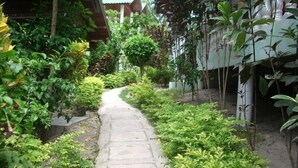 A stone pathway flanked by lush greenery and a building with a corrugated metal roof. - Save Bungalows (Koh Tao)