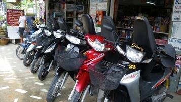 Una fila de motocicletas estacionadas frente a una tienda con un letrero que anuncia servicios como corte de libros y lavandería.