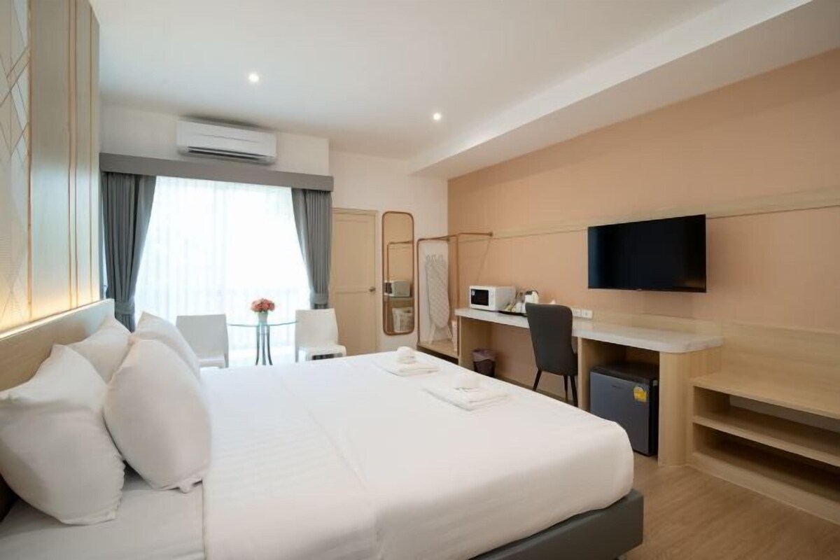 A hotel room with a bed, desk, chair, TV, and a small table with a vase.