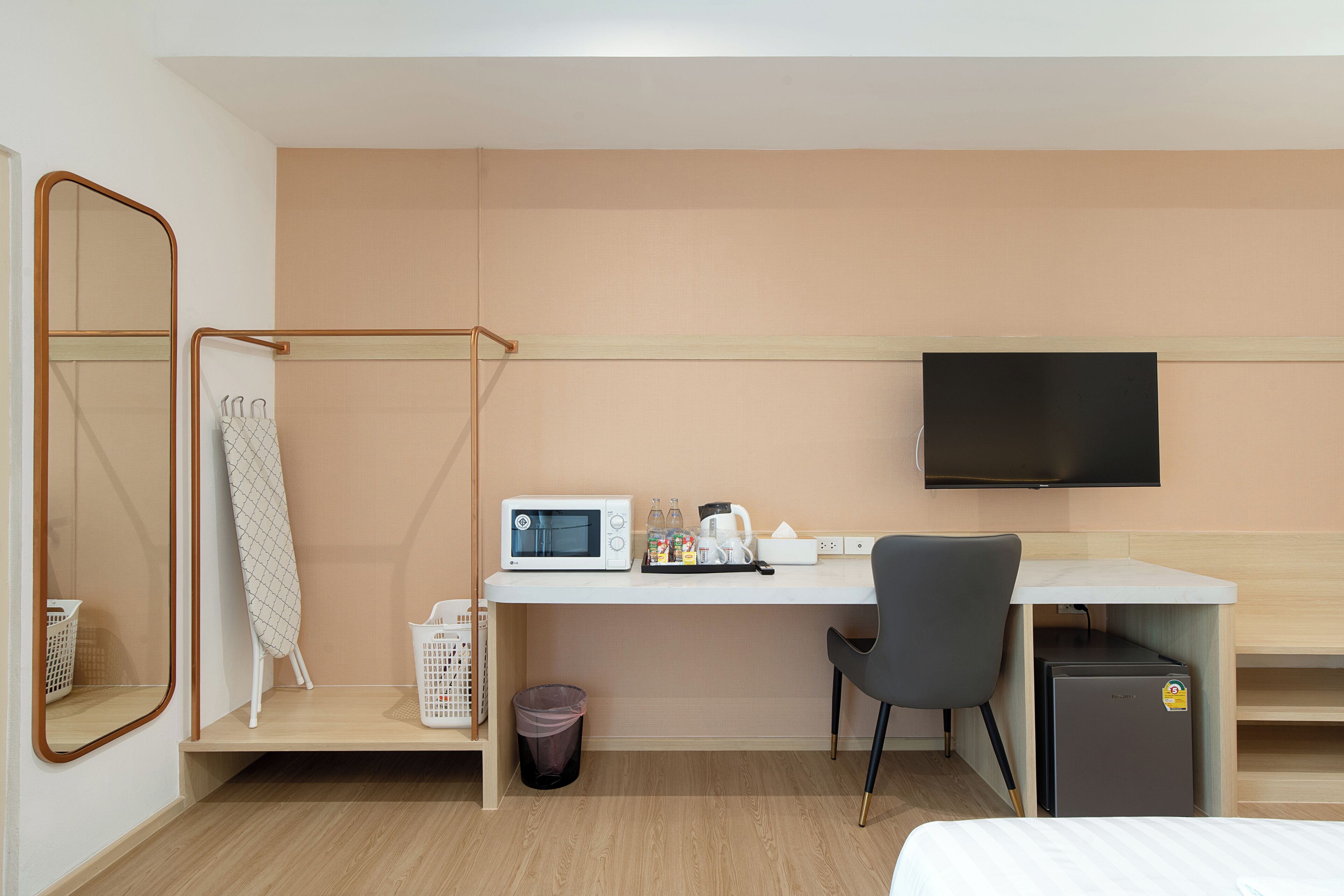 A hotel room with a bed, a desk with a computer, a microwave, a TV, and a trash bin.